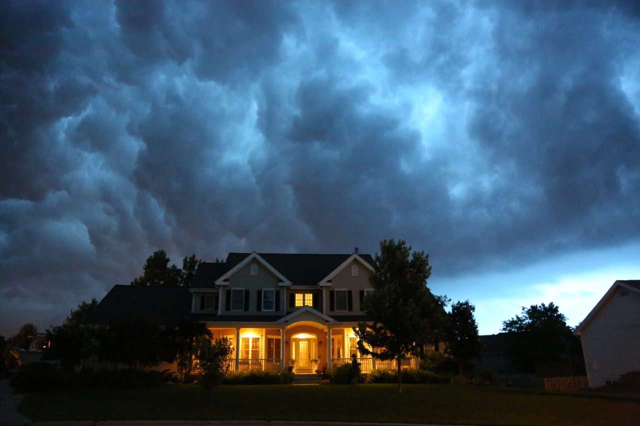 A well appointed house is lit up while a large thunderstorm moves in overhead. Ample copy space above.