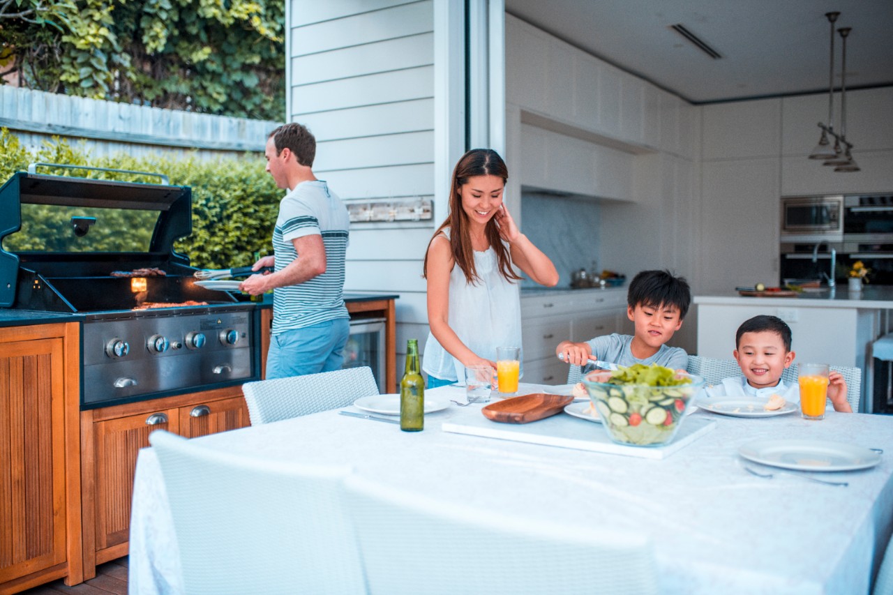 Family with two children having lunch outdoors. They are enjoying time together. Father is using barbecue grill.